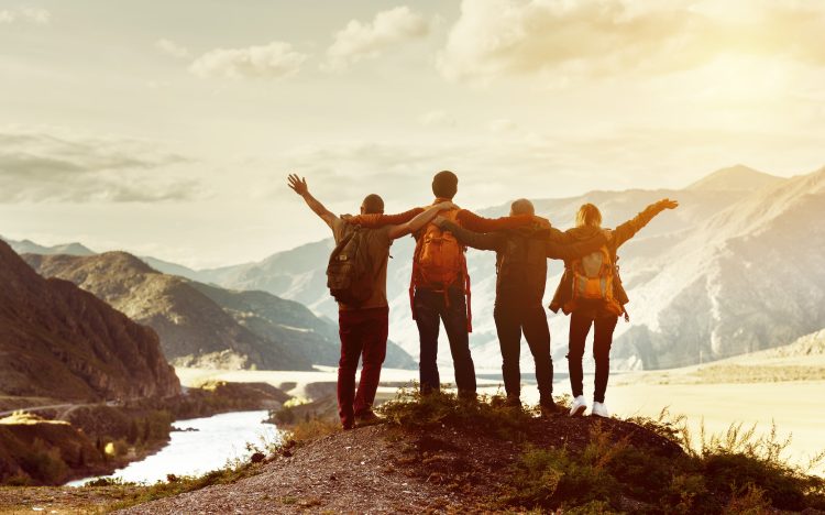 Four happy friends are looking on mountains and having fun together. Space for text. Travel concept